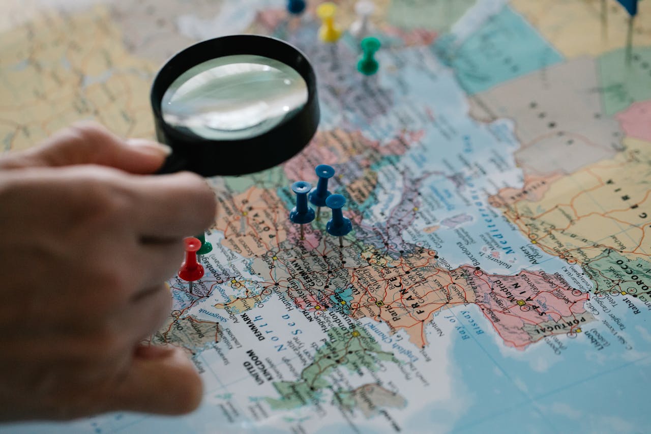 Magnifying glass focuses on pins highlighting travel destinations on a world map.